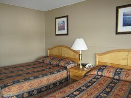Quarto de hotel com duas camas, abajur, telefone e quadros na parede.