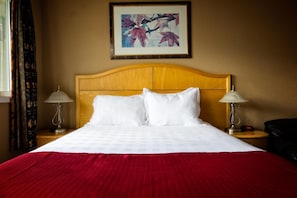 A hotel room with a wooden headboard, white bedding, two bedside lamps, and a framed artwork on the wall.