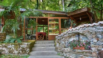 A rustic wooden structure with a stone wall and a glass door leading to a room with a red checkered tablecloth.