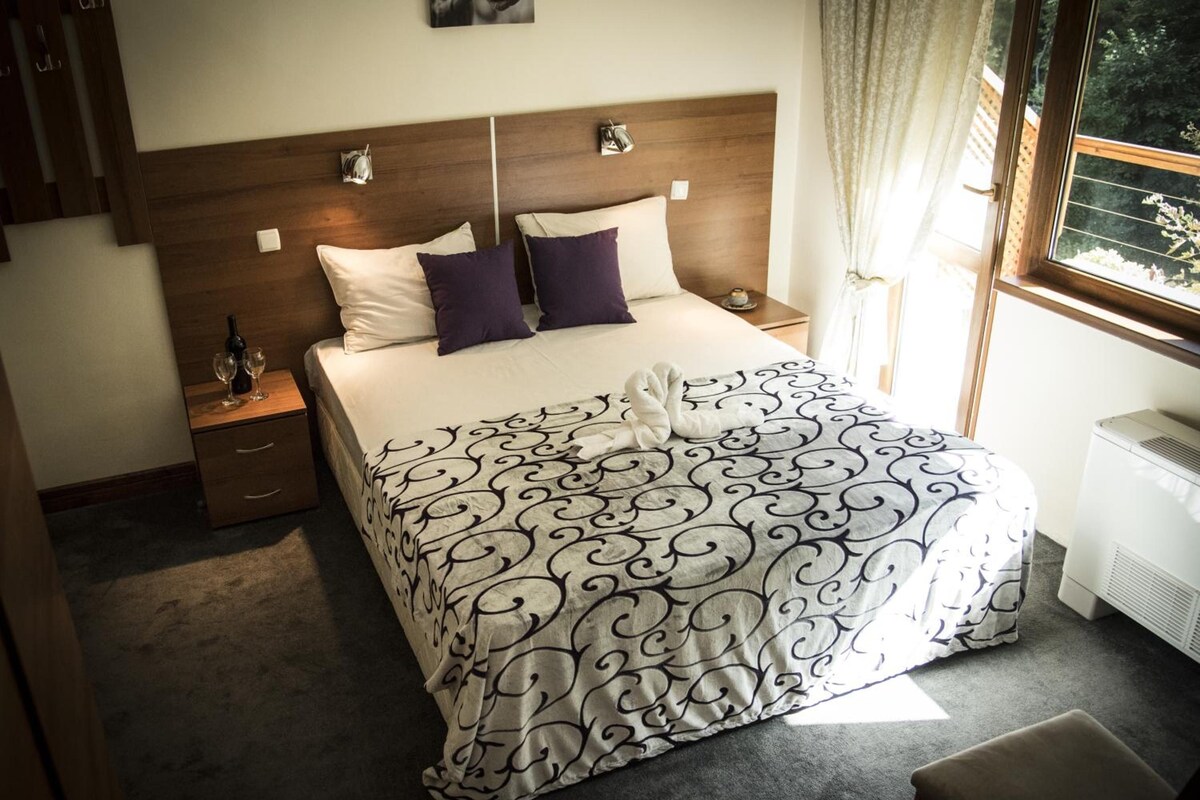 A hotel room with a bed, bedside tables, a window with curtains, and a radiator.