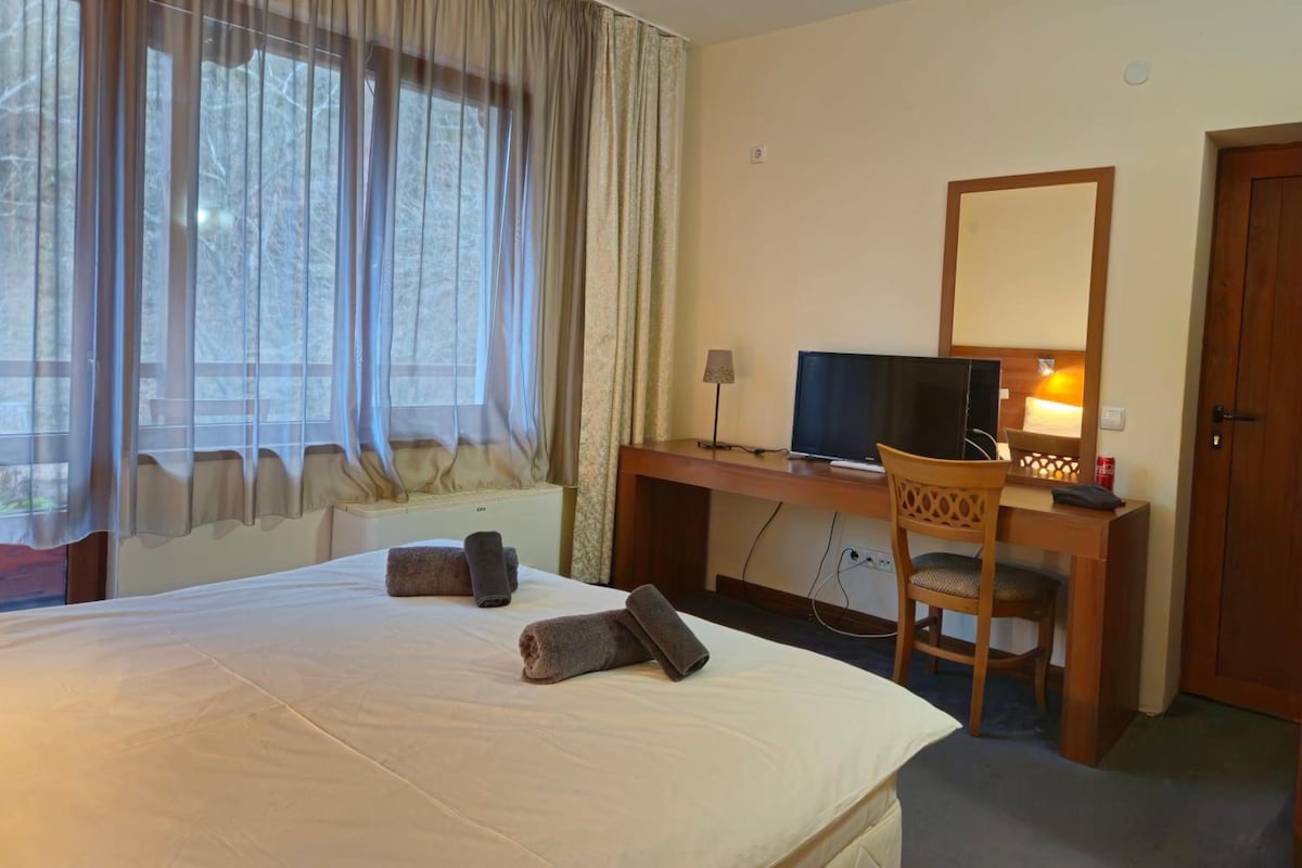 A hotel room with a bed, a desk with a computer, a chair, and a television.