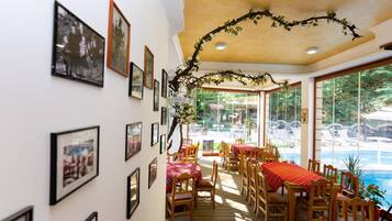 A dining area with tables and chairs, a ceiling with a decorative branch, and framed pictures on the walls.