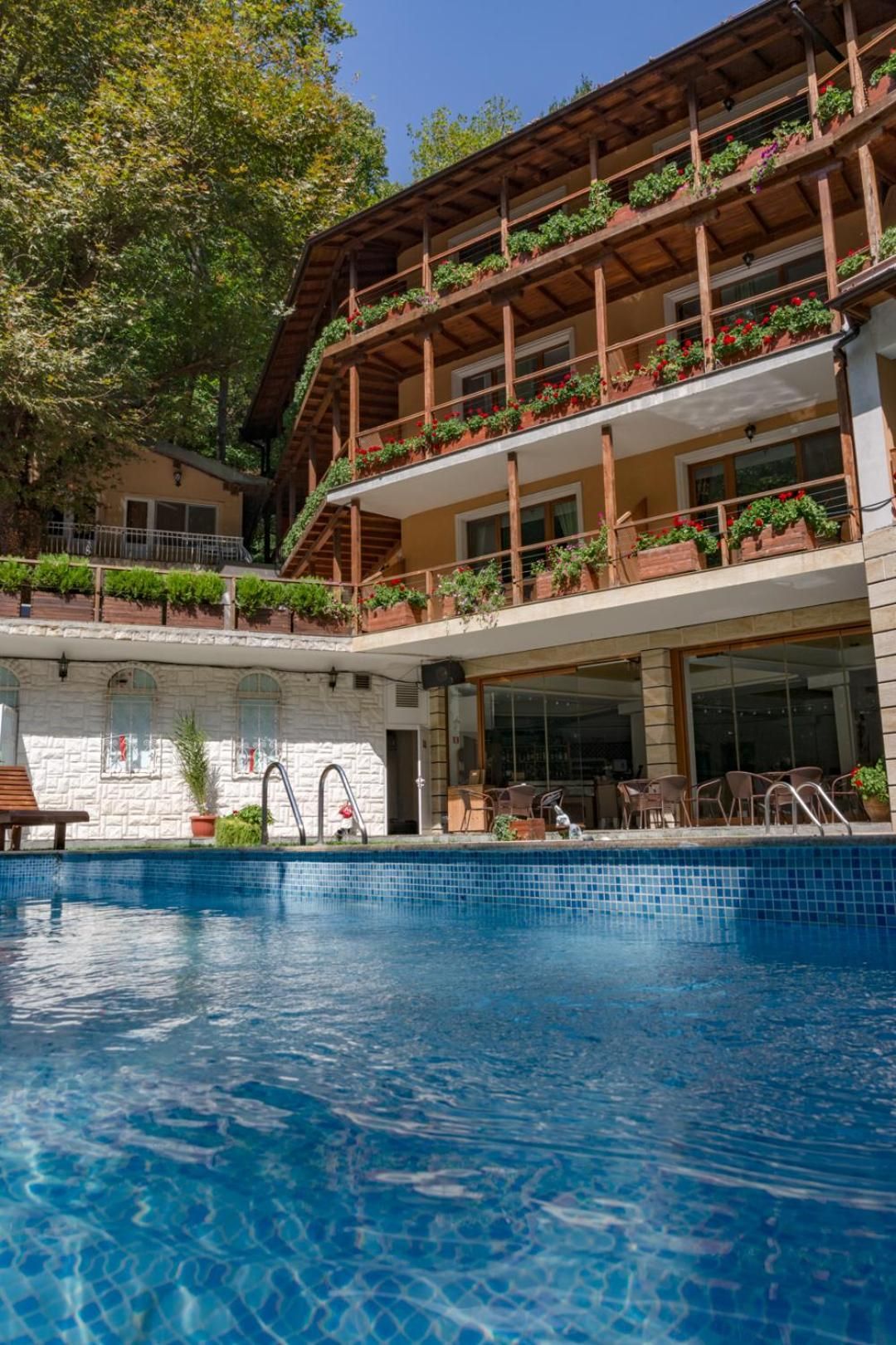 A hotel with a pool, outdoor seating, and balconies with plants.