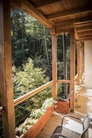 Un balcón de madera con vista a un área boscosa, barandillas de madera y una silla.