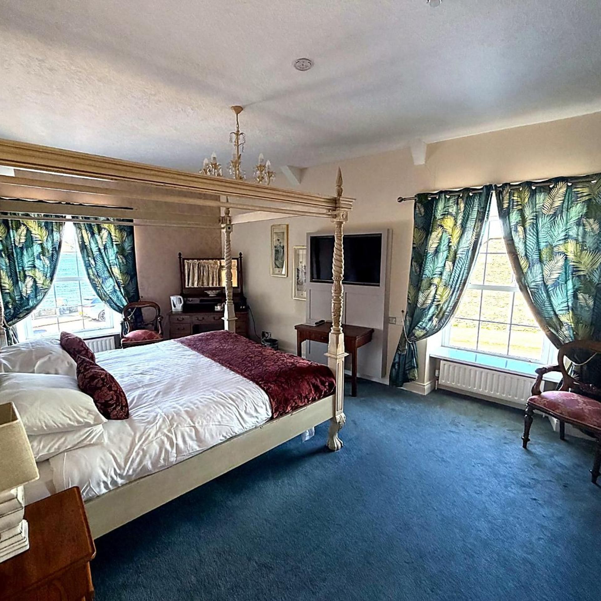 A four-poster bed with a red throw blanket, a television on the wall, and a window with curtains.