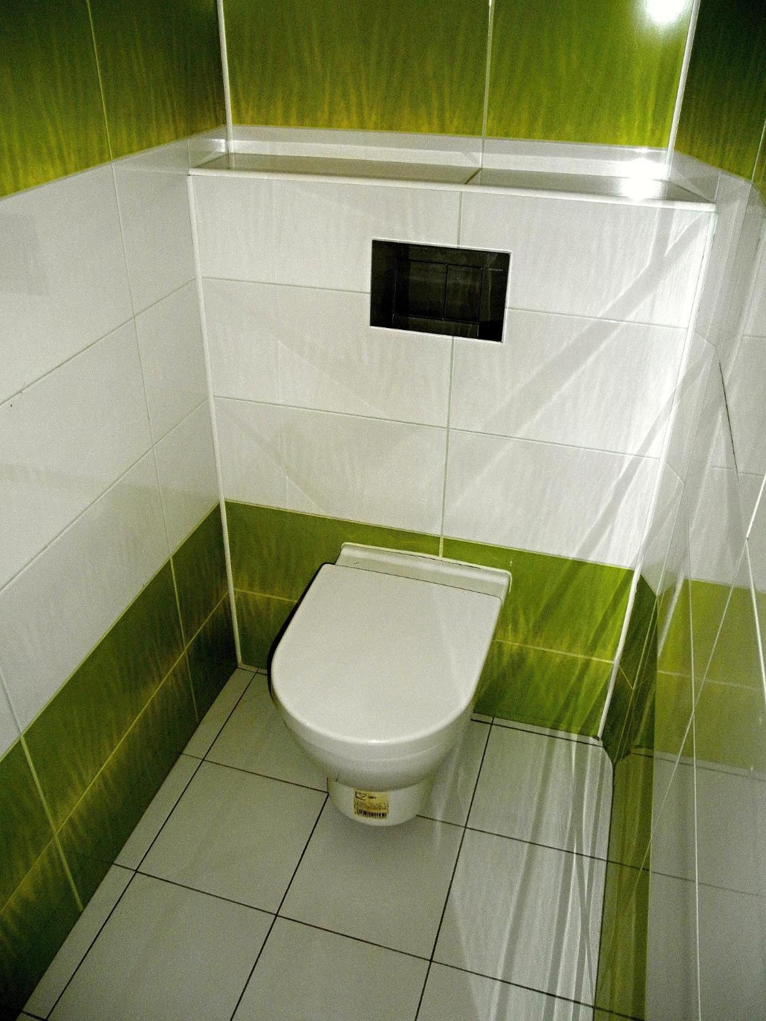 Une petite salle de bain fermée, comprenant des toilettes, un lavabo fixé au mur et des murs recouverts de carreaux verts.