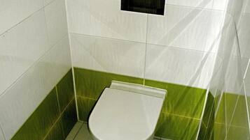 Une petite salle de bain fermée, comprenant des toilettes, un lavabo fixé au mur et des murs recouverts de carreaux verts.