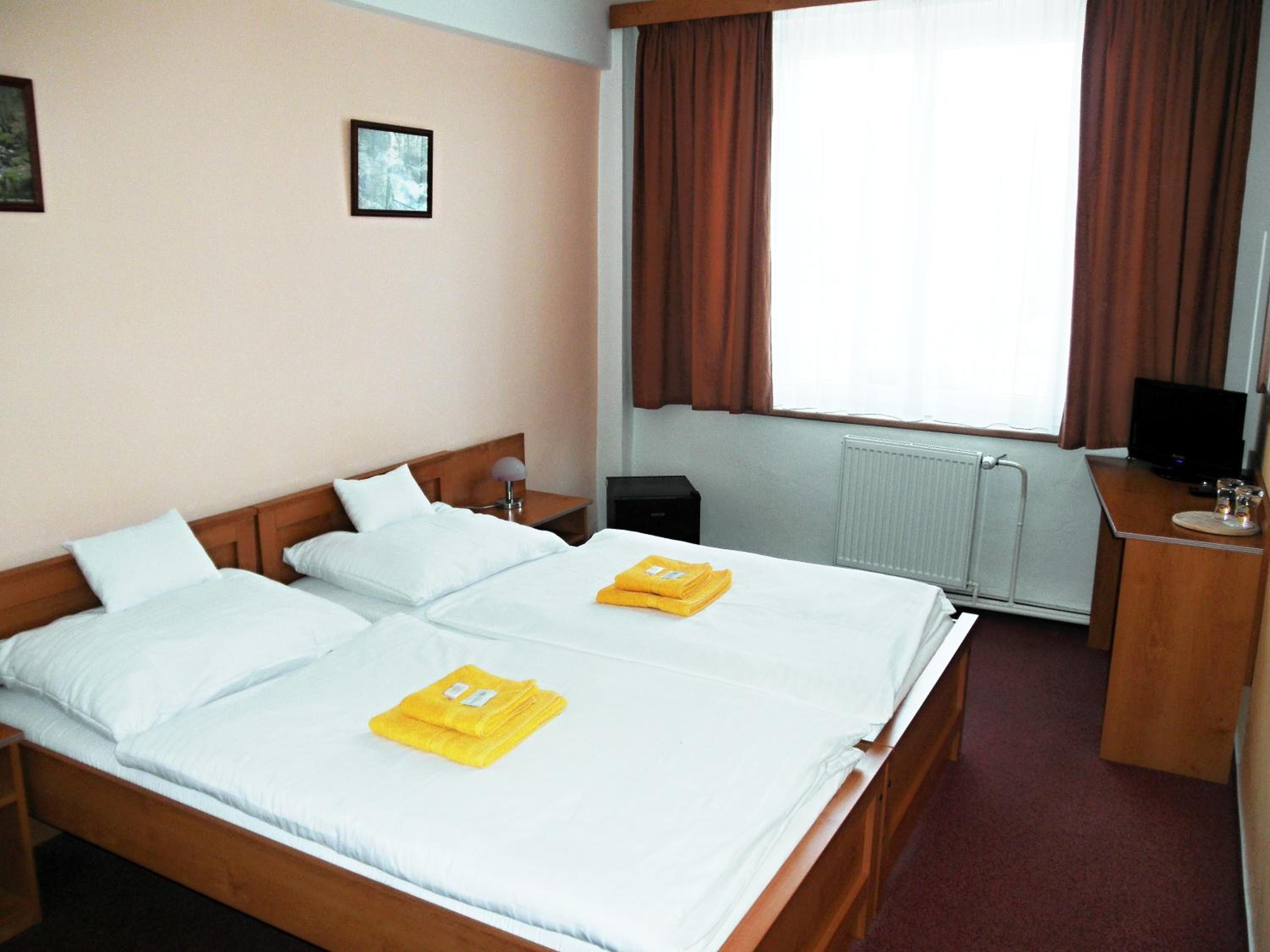 Habitación de hotel con cama doble, mesita de noche con lámpara, televisor y ventana con cortinas.