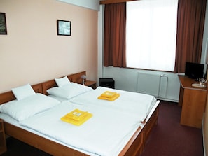 A hotel room with a double bed, a bedside table with a lamp, a television, and a window with curtains.