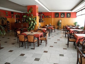 A restaurant with multiple tables and chairs, a large plant, and a clock on the wall.