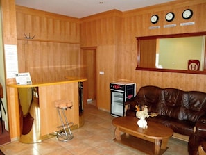 A reception area with a wooden reception desk, a brown leather sofa, a coffee table, a refrigerator, and a wall clock.