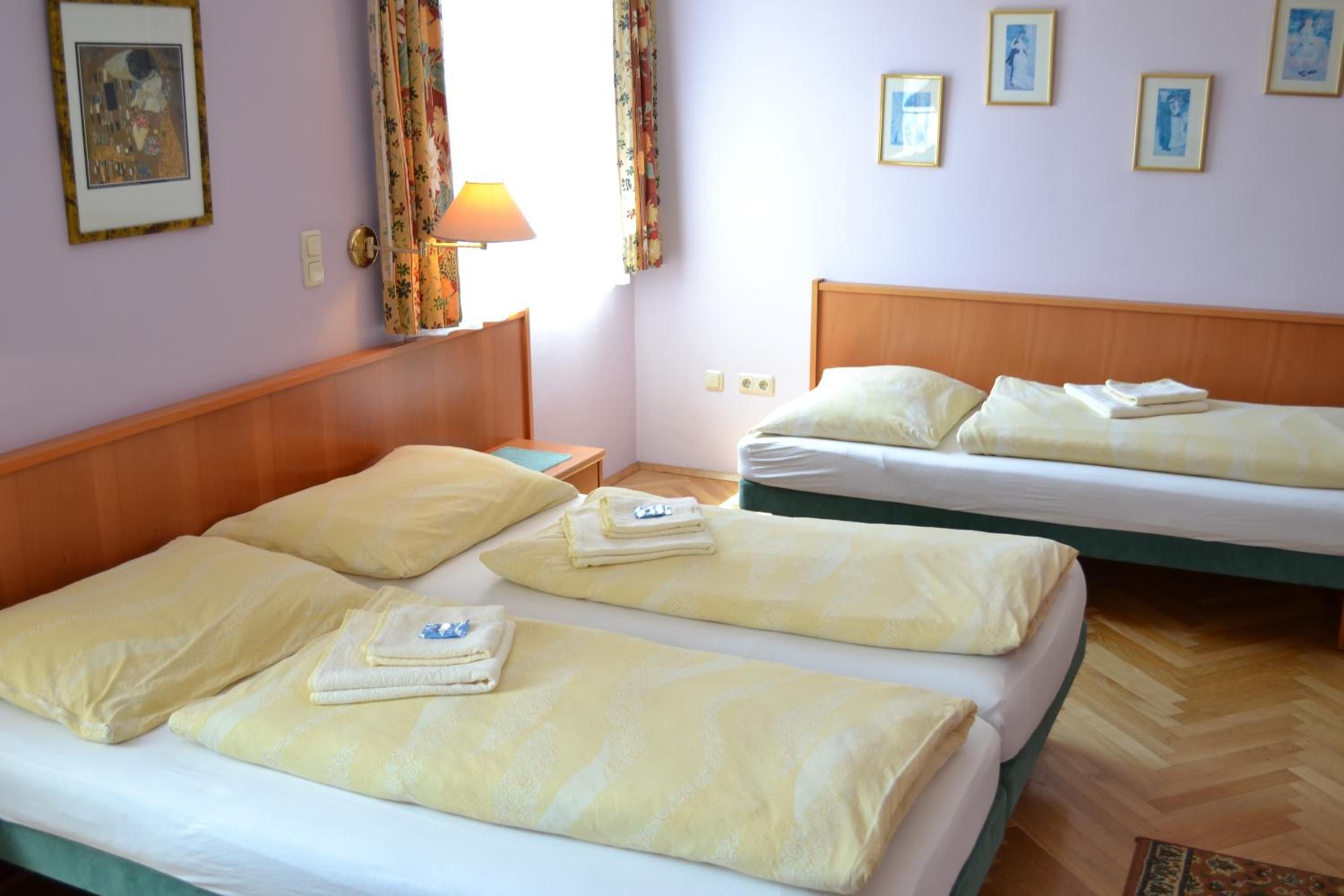 Ein Hotelzimmer mit zwei Betten, einem Nachttisch, einer Lampe und einem Fenster mit Vorhängen.