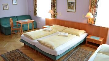 Ein Hotelzimmer mit einem Doppelbett, einem grünen Schlafsofa, einem kleinen Tisch, zwei Nachttischen und einem gemusterten Teppich.