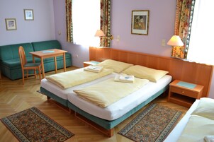 Habitación de hotel con cama doble, sofá verde, una mesita, dos mesitas de noche y un tapete estampado.