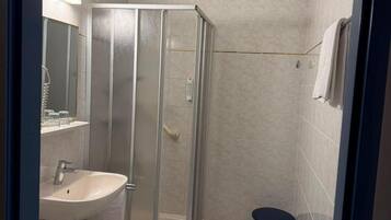 A bathroom with a shower enclosure, sink, toilet, and a small stool.