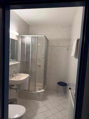 Un baño con cabina de ducha, lavabo, inodoro y un taburete pequeño.