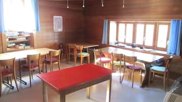 Ein Zimmer mit Holzwänden, einem roten Tisch, mehreren Stühlen, einem Bücherregal und einem Fenster mit Vorhängen.