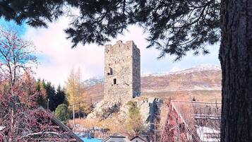 Ein historischer Steinturm mit einem Hotel und Restaurant im Vordergrund, umgeben von verschneitem Gelände und Bäumen.