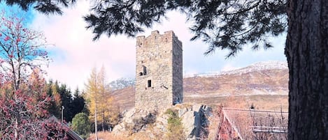 A historic stone tower with a hotel and restaurant in the foreground, surrounded by snow-covered ground and trees.