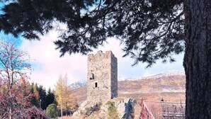 A historic stone tower with a hotel and restaurant in the foreground, surrounded by snow-covered ground and trees. - Jugendherberge Hospental (Hospental)
