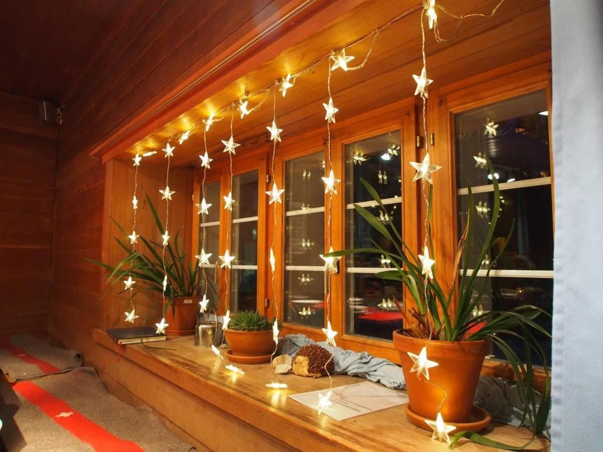 A wooden cabin with a porch decorated with string lights and potted plants.