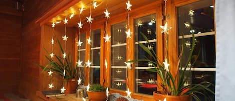 A wooden cabin with a porch decorated with string lights and potted plants.
