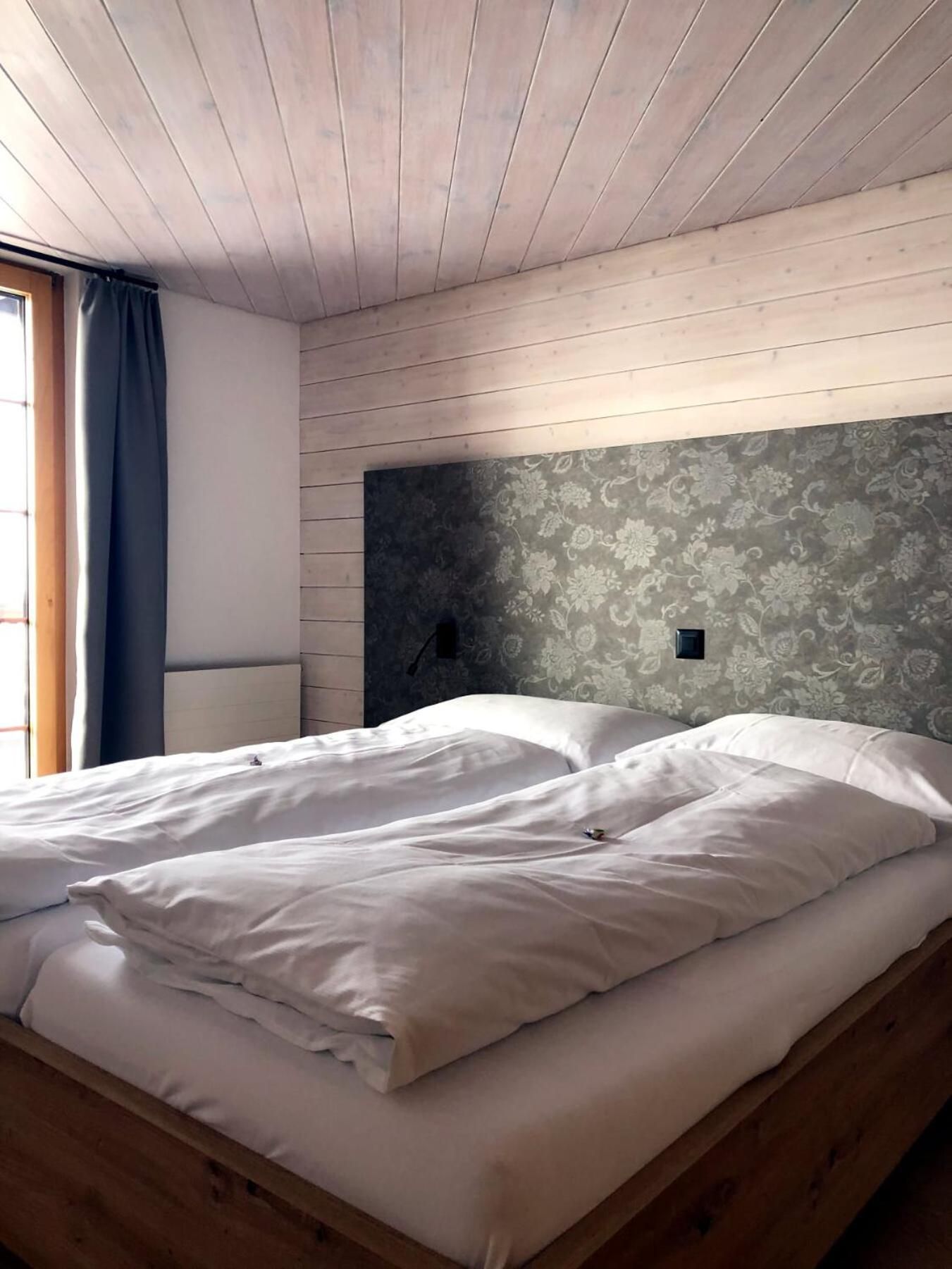 A room with a bed, wooden headboard, and a window with curtains.