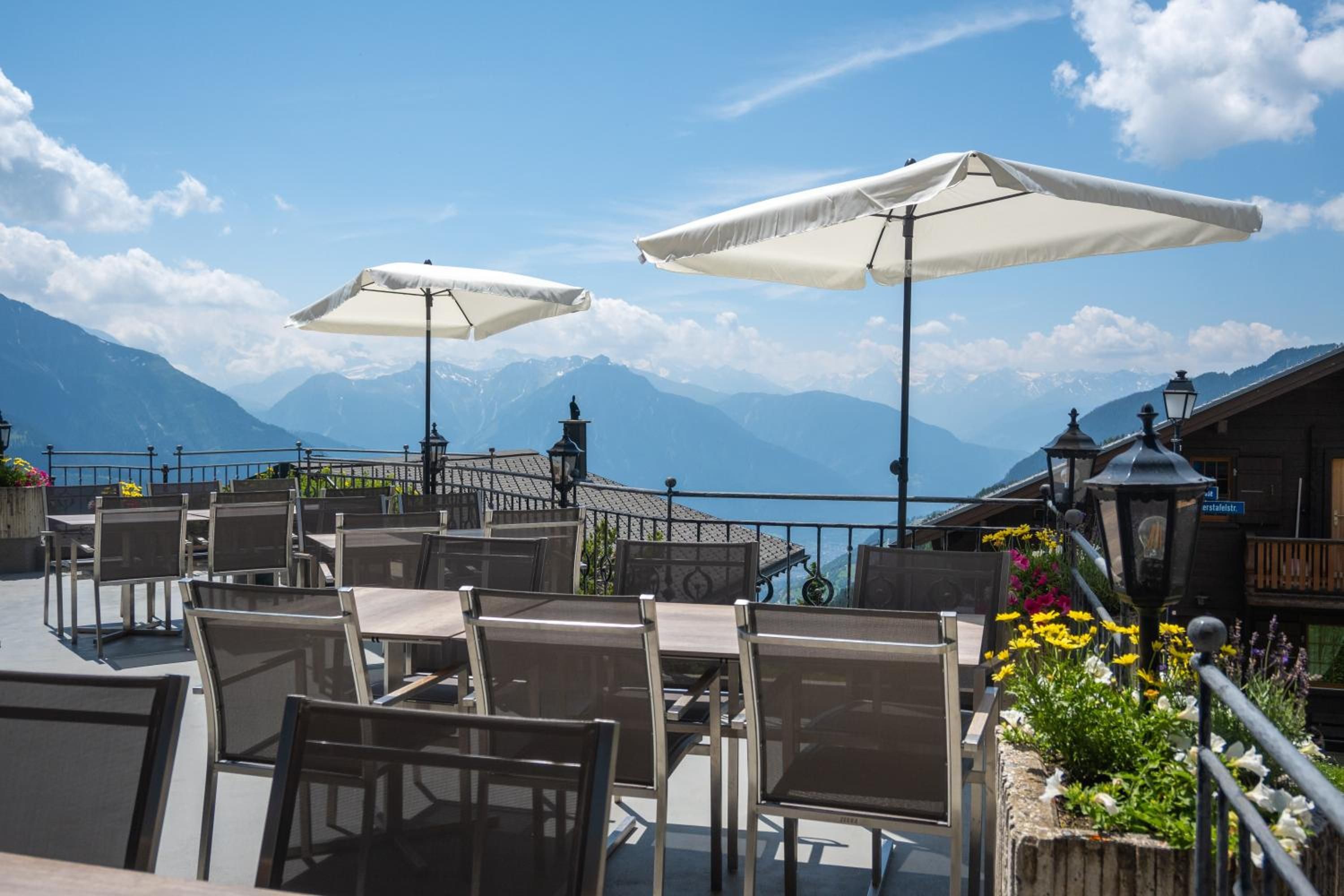 Outdoor seating with umbrellas, a mountain view, and a railing.