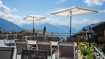 Outdoor seating with umbrellas, a mountain view, and a railing.