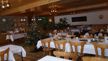 A dining area with wooden tables and chairs, a Christmas tree, and a stone wall with shelves.