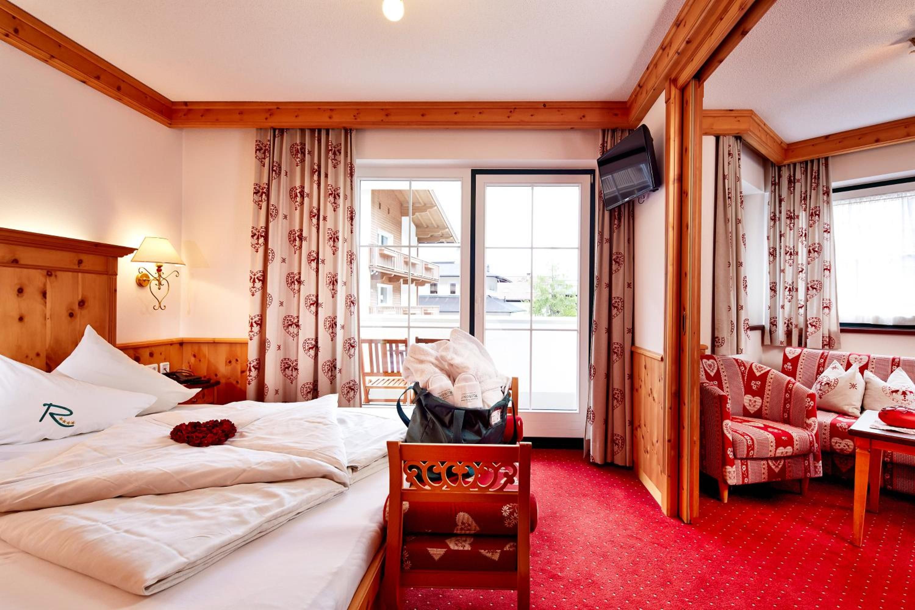 A hotel room with a bed, a chair, a sofa, a TV, and a window with curtains.