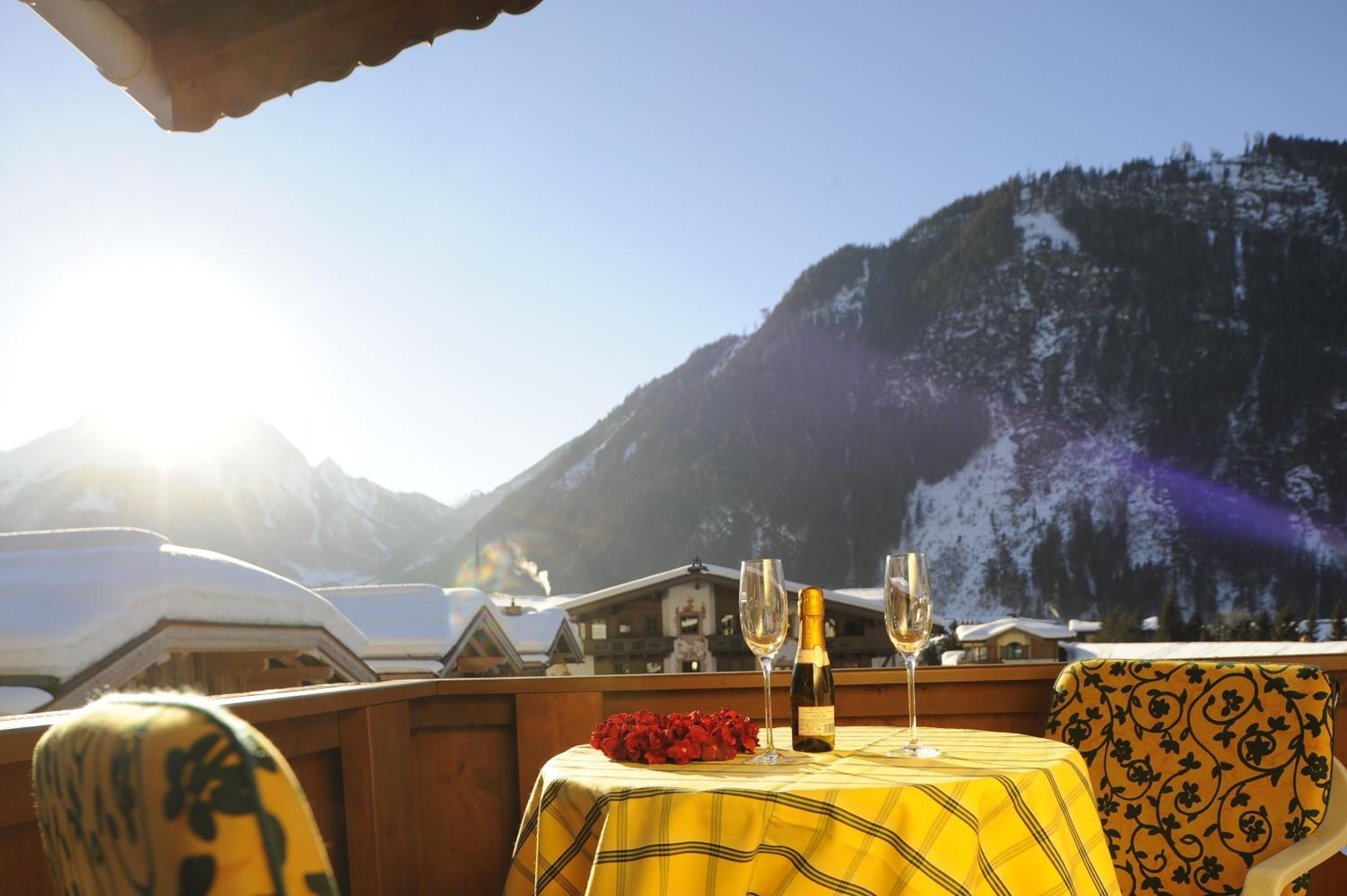 A table with a yellow tablecloth, two wine glasses, and a bottle of wine, set against a mountainous backdrop.
