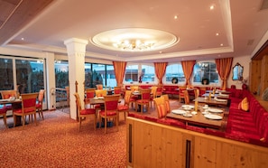 En restaurang med flera olika sittområden, inklusive avskilda bås och bord, med heltäckningsmatta på golvet och stora fönster.