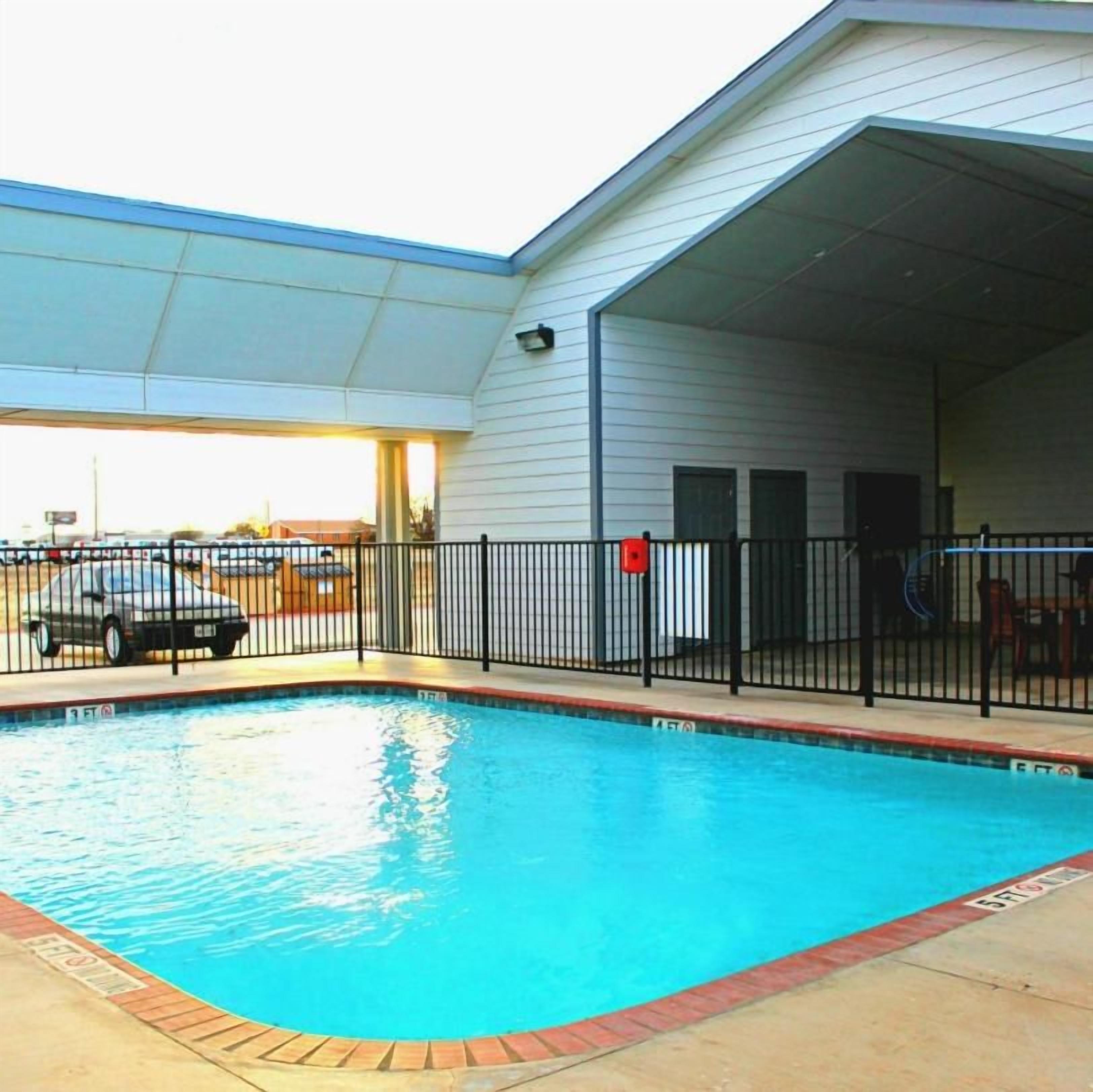 A swimming pool with a fenced area, a covered parking section, and a building with a flat roof.