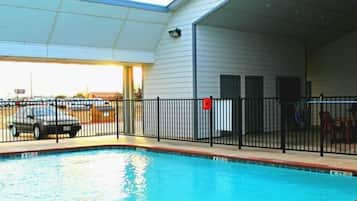 A swimming pool with a fenced area, a covered parking section, and a building with a flat roof.