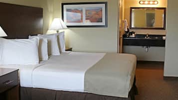 A hotel room with a bed, a nightstand, a lamp, a framed picture on the wall, and a bathroom with a mirror and sink.
