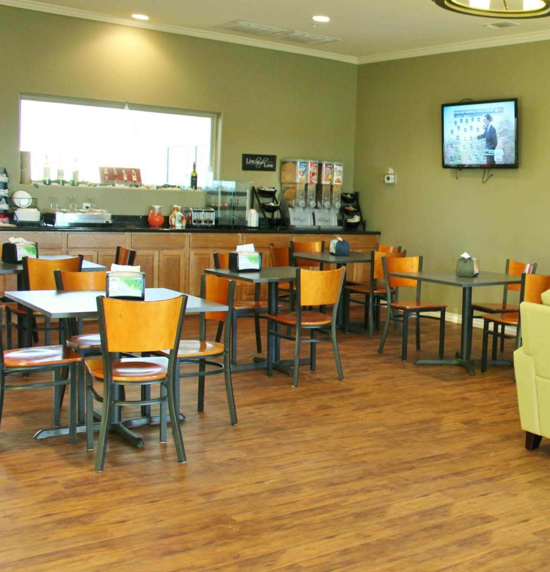 A restaurant with wooden tables and chairs, a coffee bar, and a television mounted on the wall.