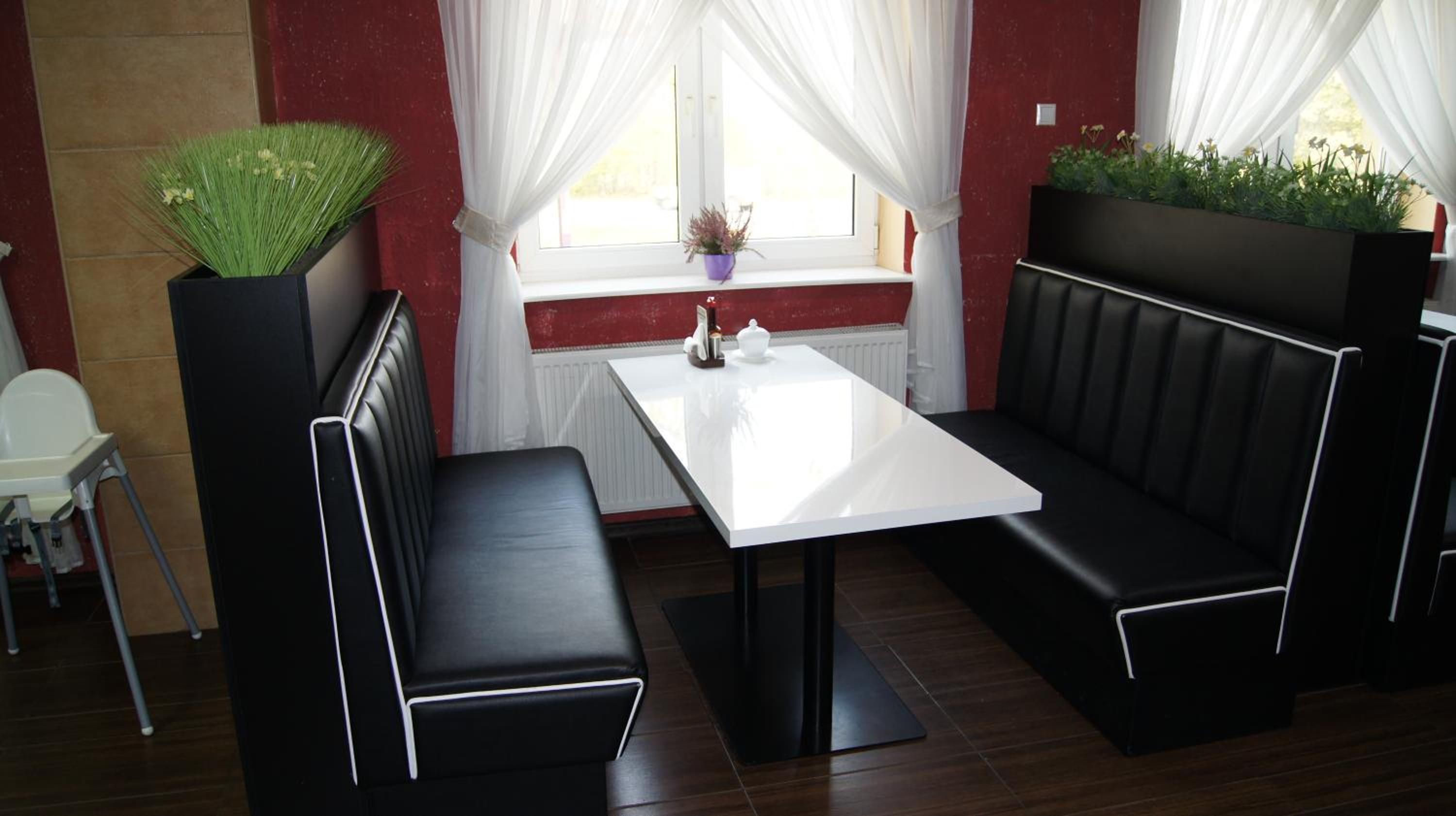 A modern dining area with a white table, black cushioned seating, and potted plants.