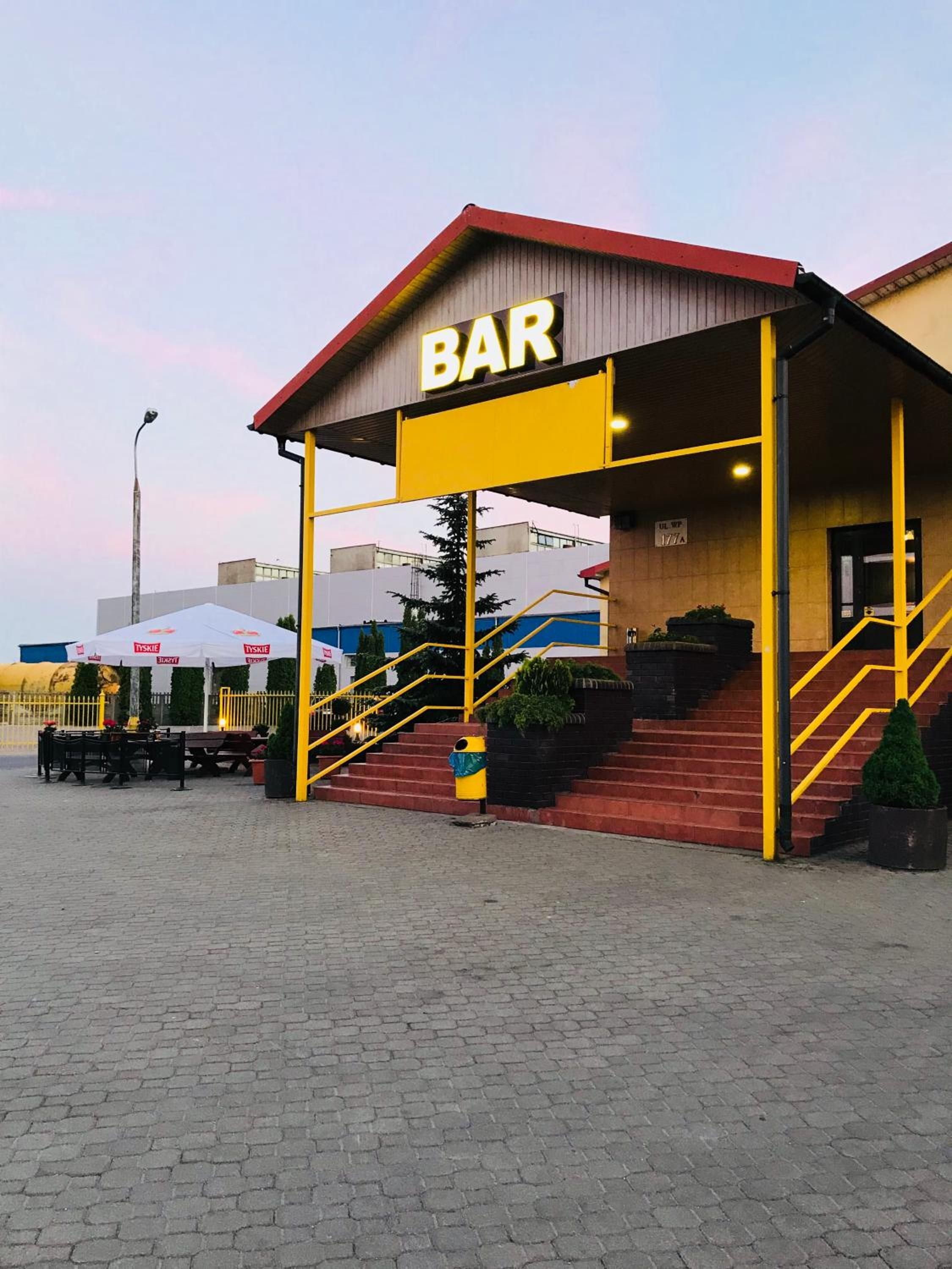 A bar with a red roof and yellow accents, outdoor seating, and a staircase leading to the entrance.