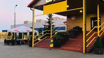 A bar with a red roof and yellow accents, outdoor seating, and a staircase leading to the entrance.