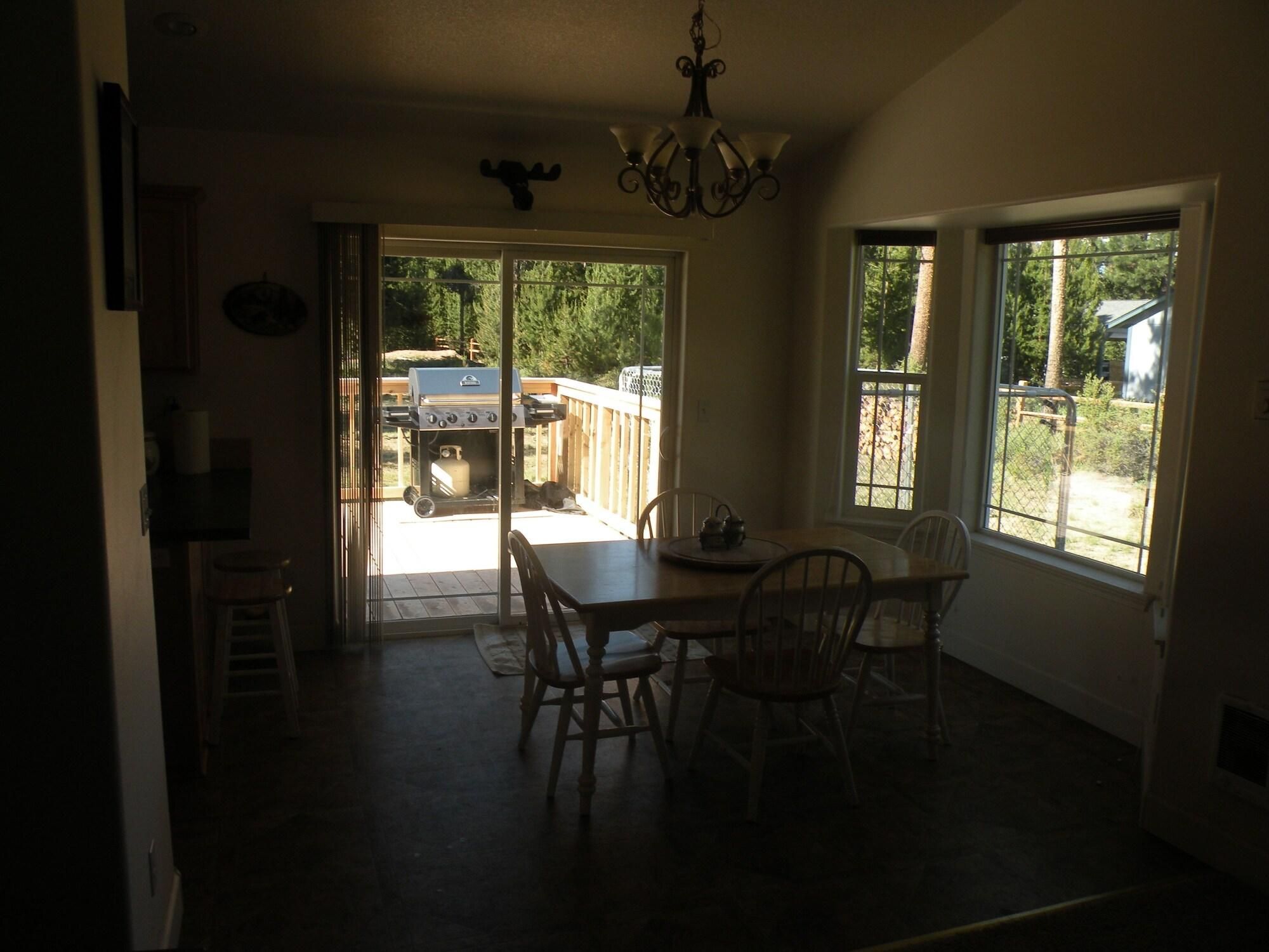 A dining area with a table and chairs, a chandelier, and a view through a glass door to an outdoor grill area.