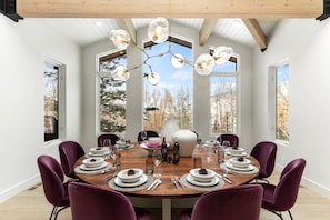 A dining room with a round table set for six, surrounded by purple chairs, with a large window providing a view of trees and mountains. - Wonderland Estate 6 Bedrooms Pas-2680 By Kbm (Park City)