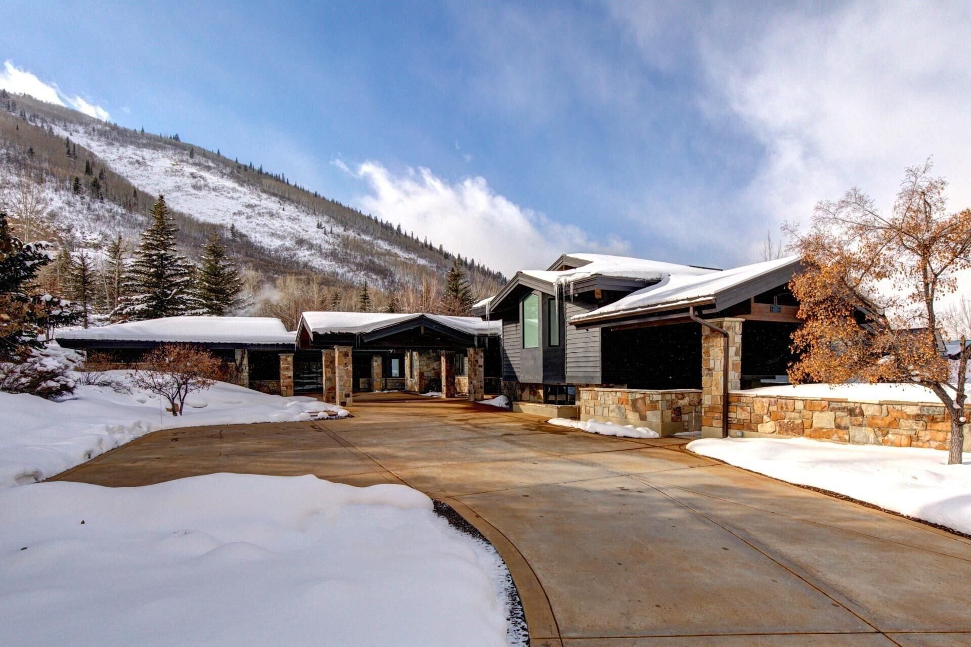 A modern building with a stone facade and a covered driveway, surrounded by snow-covered ground and trees.