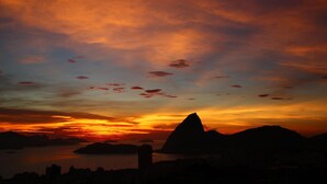 Ein Sonnenuntergang über einer Berglandschaft mit der Silhouette eines Berggipfels und einem Gewässer.