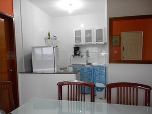 Una cuina compacta amb armaris blancs, nevera, cafetera i un mantell de taula blau amb dibuixos.