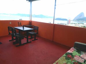 Un balcó amb taula i cadires, un paviment vermell i una vista d'un paisatge urbà amb una muntanya destacada.