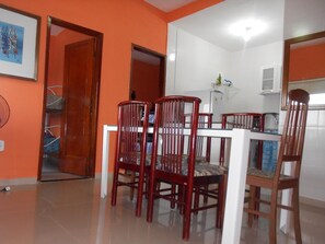 A dining area with a white table and red chairs, a kitchen with white cabinets, and a door leading to another room. - Hostel Tavares Bastos (Rio de Janeiro)