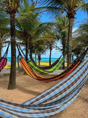 Uma rede esticada entre palmeiras em uma praia arenosa, com vista clara para o oceano.