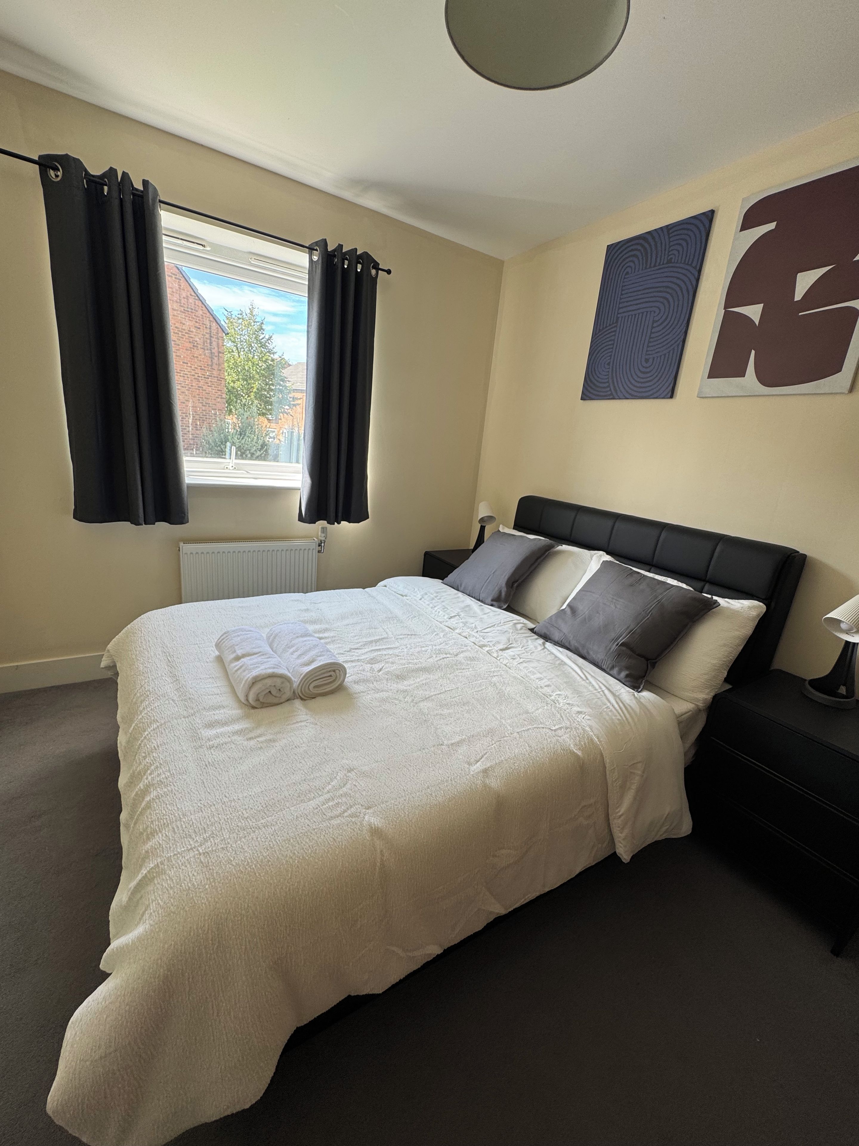 A bedroom with a large bed, a nightstand, a lamp, and a window with curtains.