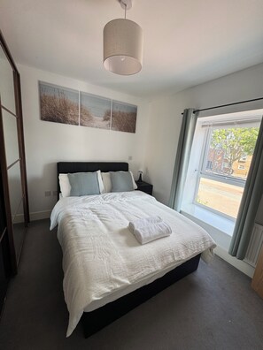A bedroom with a bed, a bedside table, a lamp, a window with curtains, and artwork on the wall. - Modern 3Bedroom House, Garden, Free Parking, Sleeps 7, Easy Central London Reach (Orpington)